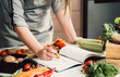 © Tijana - Unrecognizable woman is looking for recipes in cookbook.Female chef reading recipes in book and holding pen on table full with fresh vegetables for healthy lunch