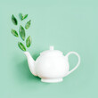 top view of white teapot and tea leaves on green background