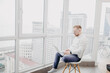 © velimir - man sitting in a chair with a laptop by the window, the concept of self-isolation and online work