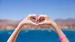 © Natallia - Female hands in the shape of heart on background of blue sea, mountains and sky. Travel, tourism, relax and happiness concept. Selective focus.