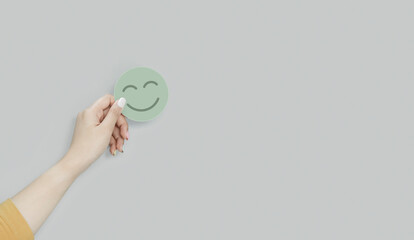 Wall Mural - Hand holding green paper cut happy smile face, positive thinking, mental health assessment , world mental health day concept