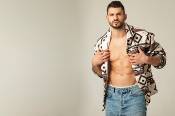 Muscle strong beautiful stripped male model shirtless in denim jeans and etno jacket on grayisolated font background