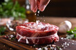 © amenic181 - Hand sprinkling salt on fresh raw beef meat on a cutting board