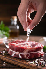 Wall Mural - Hand sprinkling salt on fresh raw beef meat on a cutting board