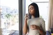 © Wavebreak Media - Mixed race transgender woman standing looking out of window holding cup of coffee