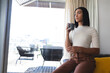 © Wavebreak Media - Mixed race transgender woman sitting in living room looking out of window holding cup of coffee