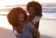 Smiling African American Mother Carrying Her Daughter Piggyback At The Beach Smiling