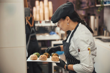 Qualified confectioner taking freshly-baked dessert scones out of oven