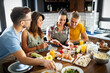 © NDABCREATIVITY - Group of happy friends laughing and talking while preparing meals in kitchen