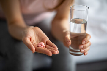 Wall Mural - Coronavirus prevention and treatment concept. Closeup view of young woman taking pills with water at home