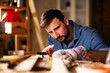 © JustLife - Young male carpenter working in workshop. Woodworker measuring wooden plank..