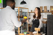 © Vadim Pastuh - Friendly and helpful waitress is serving an African-American male customer, preparing and giving paper cup of coffee to multiracial guy. Woman in apron holds out take-away coffee to guest of cafe