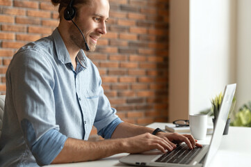 a confident male office worker sitting at the desk with a laptop, using headset communicating with c