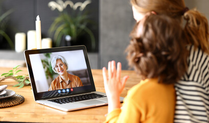 Mom and child making talking with grandma through video call on laptop