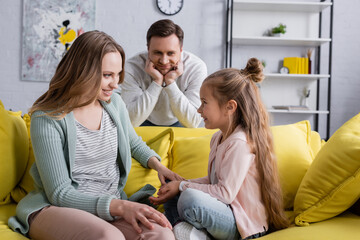 Wall Mural - Smiling girl sitting near mother and blurred father in living room.