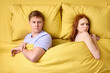 Top view on man and woman ignoring each other lying on bed, back to back