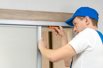 Wall Mural - Handyman who installs sliding doors at home in overalls with a screwdriver in his hands repairs the door