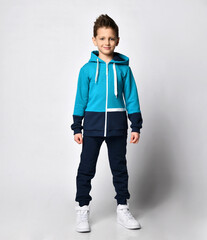 Fashion boy child in warm sportswear suit standing on studio. Male kid advertising sportive outerwear clothing. Sportive outfit for children. Studio shot portrait on grey background