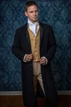 A Handsome Regency Gentleman Wearing A Gold Waistcoat, Breeches, And A Black Long Jacket And Standing In A Room With Blue Wallpaper And A Wooden Floor