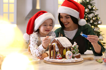 Sticker - Mother and daughter decorating gingerbread house at table indoors