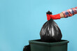Man throwing garbage bag into bin on light blue background, closeup. Space for text