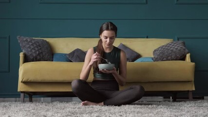 Wall Mural - Sporty woman eating cereals on the floor after fitness session at home