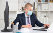 © JackF - Young man entrepreneur in protective face mask working alone on laptop at his workplace
