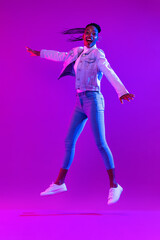 Wall Mural - Trendy stylish energetic young African American woman jumping in futuristic purple cyberpunk neon light background