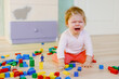 © Irina Schmidt - Upset crying baby girl with educational toys. Sad tired or hungry alone healthy child sitting near colorful different wooden blocks at home or nursery. Baby missing mother in daycare