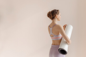 Girl with a sports mat is preparing for workout. Young woman on a beige one ton background.