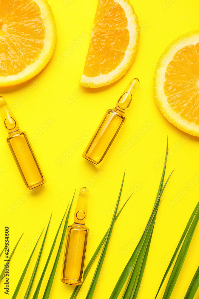 Ampules with vitamin C injection and orange fruit slices on color background