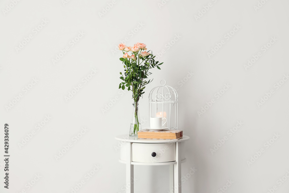 Bedside table with flowers, cup of coffee and decor near white wall