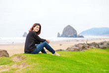 Biracial Teen Girl Sitting Near Ocean In Pacific Northwest