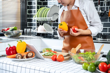 Poster - Asian housewife holding bell pepper and tomato in hands during watching tutorial cooking class online on tablet