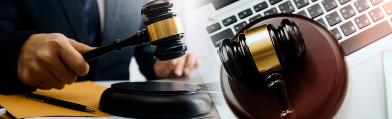 Justice and law concept.Male judge in a courtroom with the gavel, working with, computer and docking keyboard, eyeglasses, on table in morning light