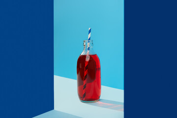 Wall Mural - Refreshing cranberrie lemonade cocktail in bottle with palm leaf on blue creative background