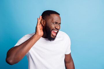 Photo of furious african man hand ear listen open mouth wear white t-shirt over blue background