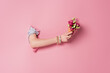 Cropped view of woman holding delicious waffle cone and rose flowers in hole of pink background