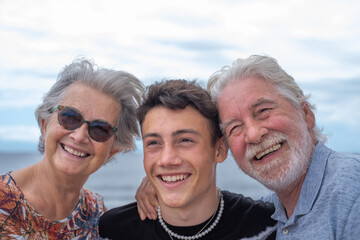 Happy group of grandparents with teenage grandson sitting outdoor at sea, hugs and smiles. Handsome people having fun together