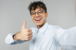Close up young smiling happy employee business latin man 20s corporate lawyer in classic white shirt glasses doing selfie shot on mobile phone show thumb up gesture isolated on grey background studio