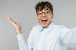 © ViDi Studio - Close up young surprised fun happy employee business latin man 20s corporate lawyer wear classic white shirt glasses doing selfie shot on mobile phone spread hand isolated on grey background studio