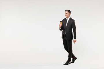 Full length side view young rich employee business corporate lawyer man in classic formal black grey suit shirt tie work in office hold paper cup coffee drink tea isolated on white background studio.