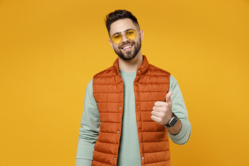 Wall Mural - Young smiling happy friendly cheerful fun caucasian man 20s wear orange vest mint sweatshirt glasses show thumb up like gesture isolated on yellow background studio portrait. People lifestyle concept.