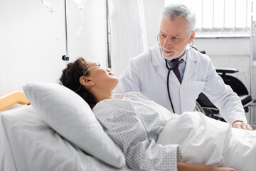 mature doctor examining african american women with stethoscope in clinic