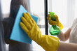 Female hands in yellow gloves wash windows with rag and cleaning agent