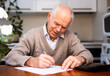 © caftor - elderly pensioner writing on piece of paper at table in kitchen