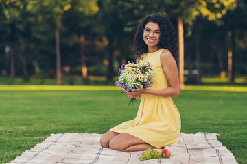 Poster - Portrait of attractive elegant cheerful girl sitting on duvet holding bouquet spending free time on fresh air outdoor