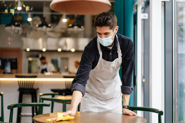 Man waiter wearing mask disinfecting table in the cafe