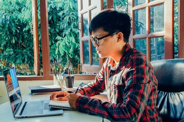 Man hand using a pencil writing notebook paper learning and researching course tutor education, online on technology personal computer laptop Are sitting on the chair people learn and work from home
