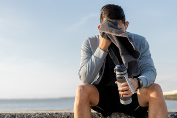 Tired man runner is resting after morning cardio outdoors and wipe the sweat his face.